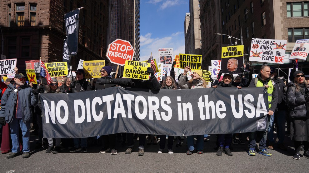 A large crowd of protesters marches through a city street carrying a prominent banner reading "No Dictators in the USA." Demonstrators hold signs including "Stop Fascism," "Arrest Trump," "Impeach. Convict. Remove.," "War Criminal," "No Tyrants," "Trump Is a Danger to Us All," and "There Can Be No Kings When the People Rise." The banner is branded with the Rise and Resist logo. Tall city buildings and a blue sky are visible in the background.
