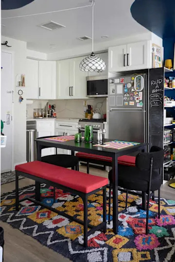 Modern kitchen with white cabinets, a black and white pendant light, red benches, and a colorful patterned rug.