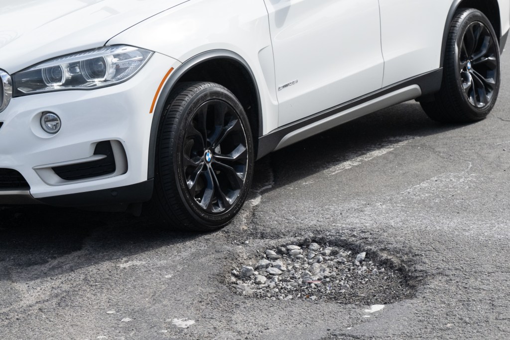 A white car parked next to a large pothole filled with gravel on Southern Boulevard in the Bronx, New York.