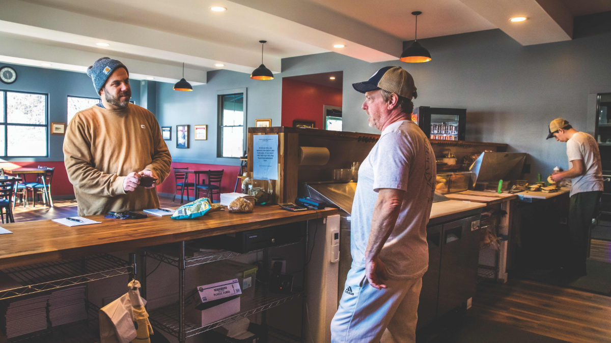 Man in baseball cap serves customer inside a deli