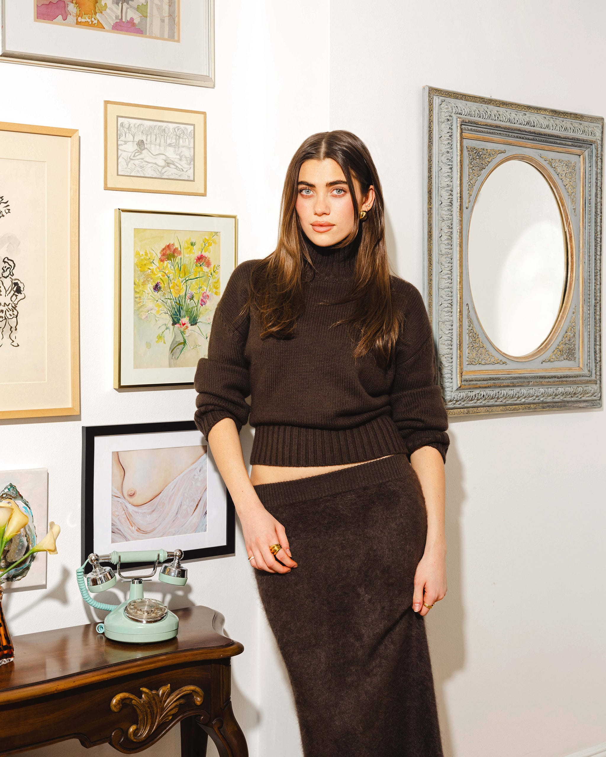 Fashionable woman in a stylish outfit stands beside a gallery wall.