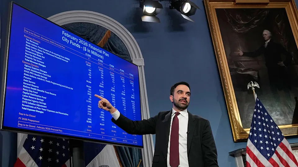 Zohran Mamdani speaking on New York City funding in front of a painting of Alexander Hamilton.