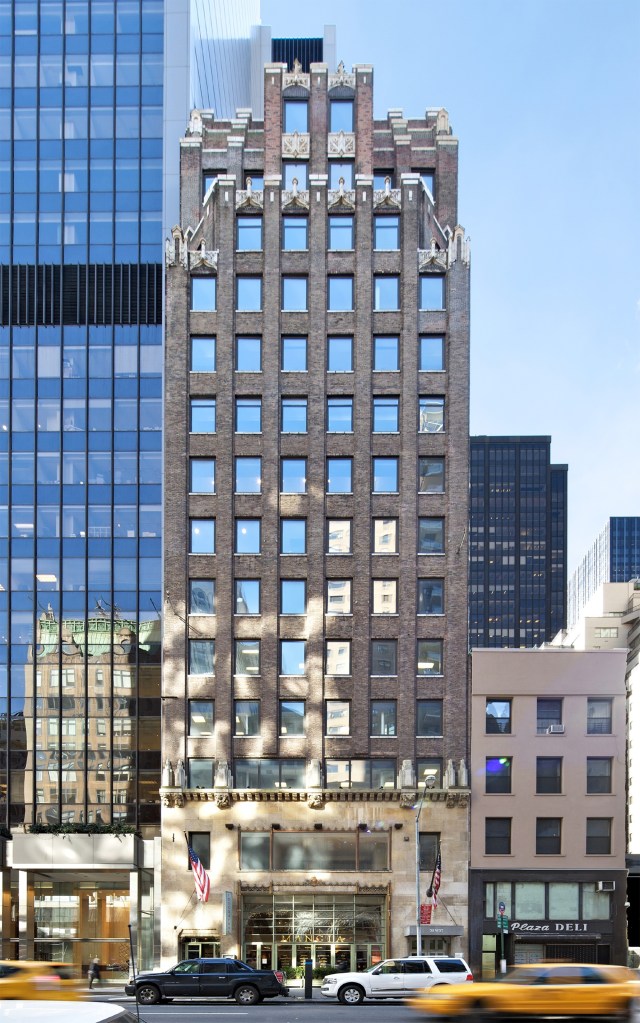 A tall, ornate brick building at 50 West 57th Street, flanked by modern glass skyscrapers and a smaller building, with traffic and parked cars in the foreground.