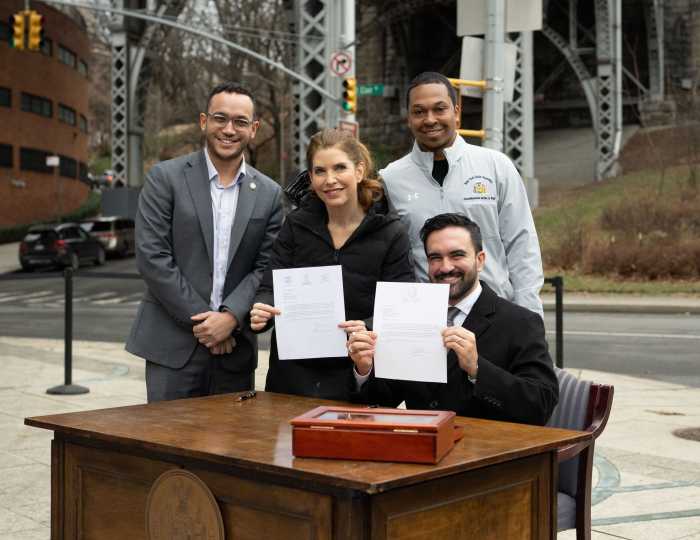 Mayor Zohran Mamdani smiling while holding signed paper with other elected officials