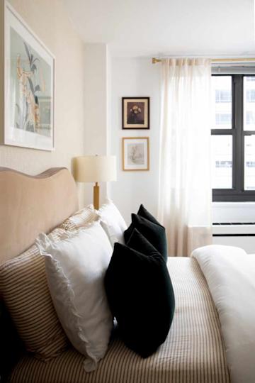 Cozy bedroom with a beige headboard, striped bedding, white and dark pillows, and framed artwork on the wall.