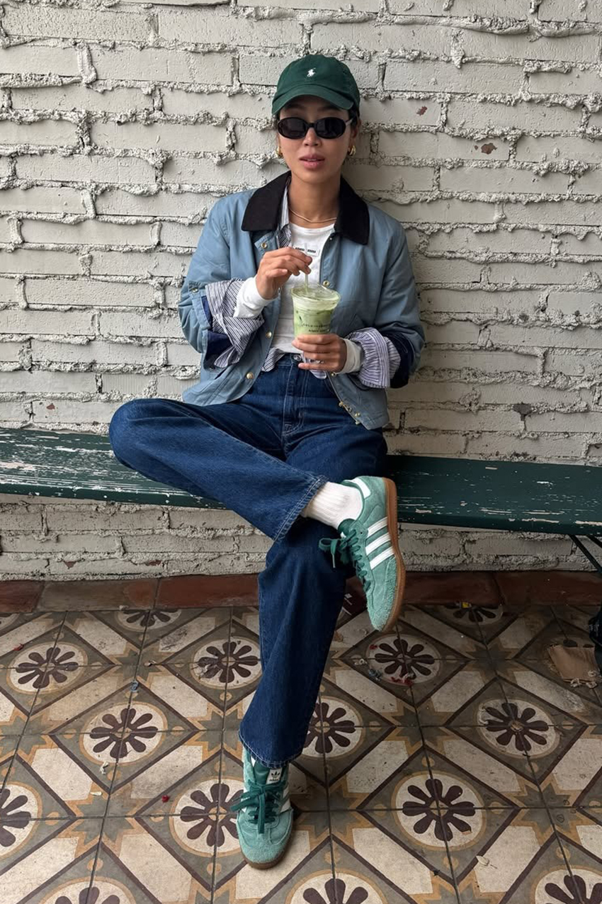 a woman wearing a green baseball cap, blue jacket, blue jeans, and green sneakers