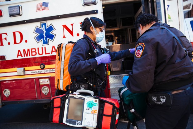 FDNY EMTs Kim Benson and Chris Feliciano carry equipment out of an ambulance outside the home of a Covid-19 patient in Queens in 2020. (Angus Mordant for New York Daily News)