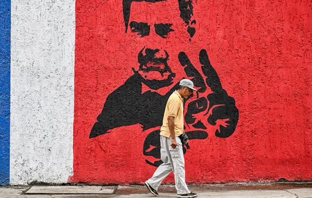 A man walks by a mural of Maduro in Caracas