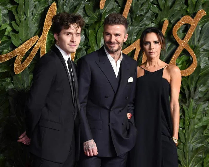 Brooklyn Beckham, David Beckham and Victoria Beckham pose on a red carpet in formal attire