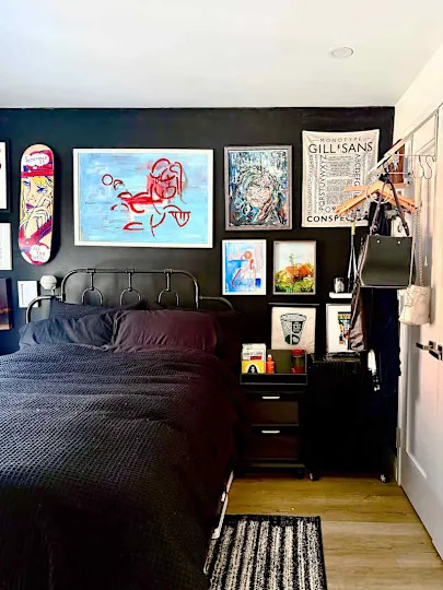 A black-themed bedroom featuring a metal bed frame, colorful artwork on the walls, and a striped rug.