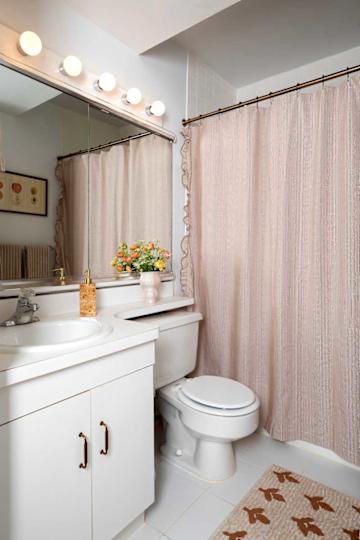 Bathroom featuring a white sink and toilet, a pink floral vase, and a shower curtain with a ruffled edge.
