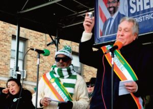 Program emcee Danny Dromm held up Malachy’s ashes during a solemn mo­ment. Looking on were Councilwoman Julie Won and Parade co-chair Archley Prudent.