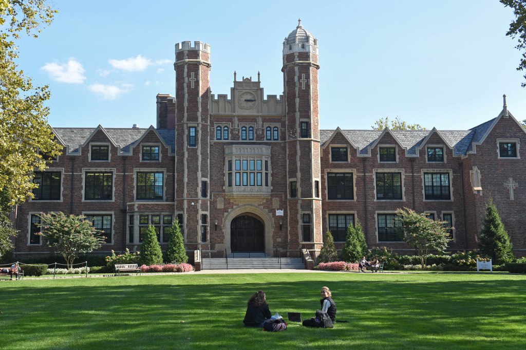 The main building at Wagner College in Staten Island, 1 Campus Road, featuring a large brick building with two prominent towers and students on the lawn.