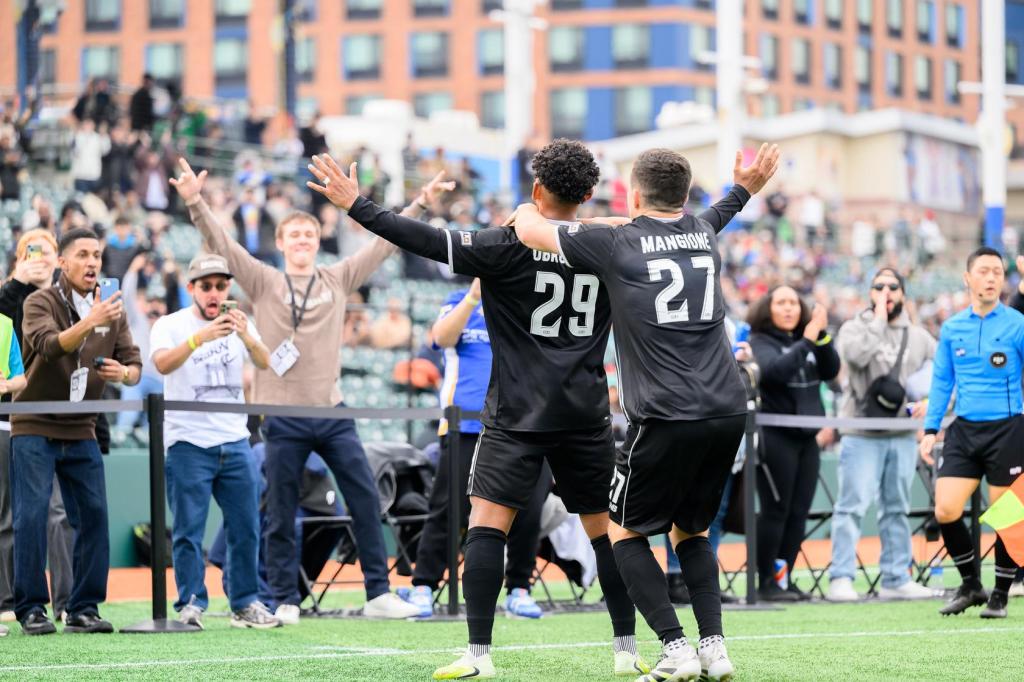 Brooklyn FC men players Juan Carlos Obregón Jr. and Peter Mangione celebrate with supporters after a goal at Maimonides Park.
