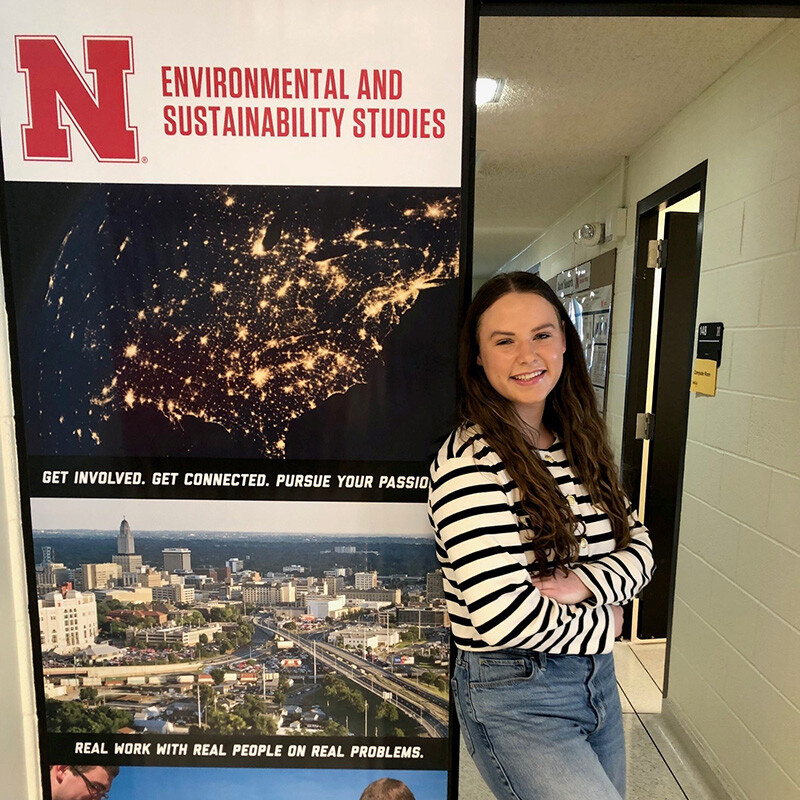 Brooklyn Buell stands next to a poster about Environmental and Sustainability Studies, the program she is enrolled in.