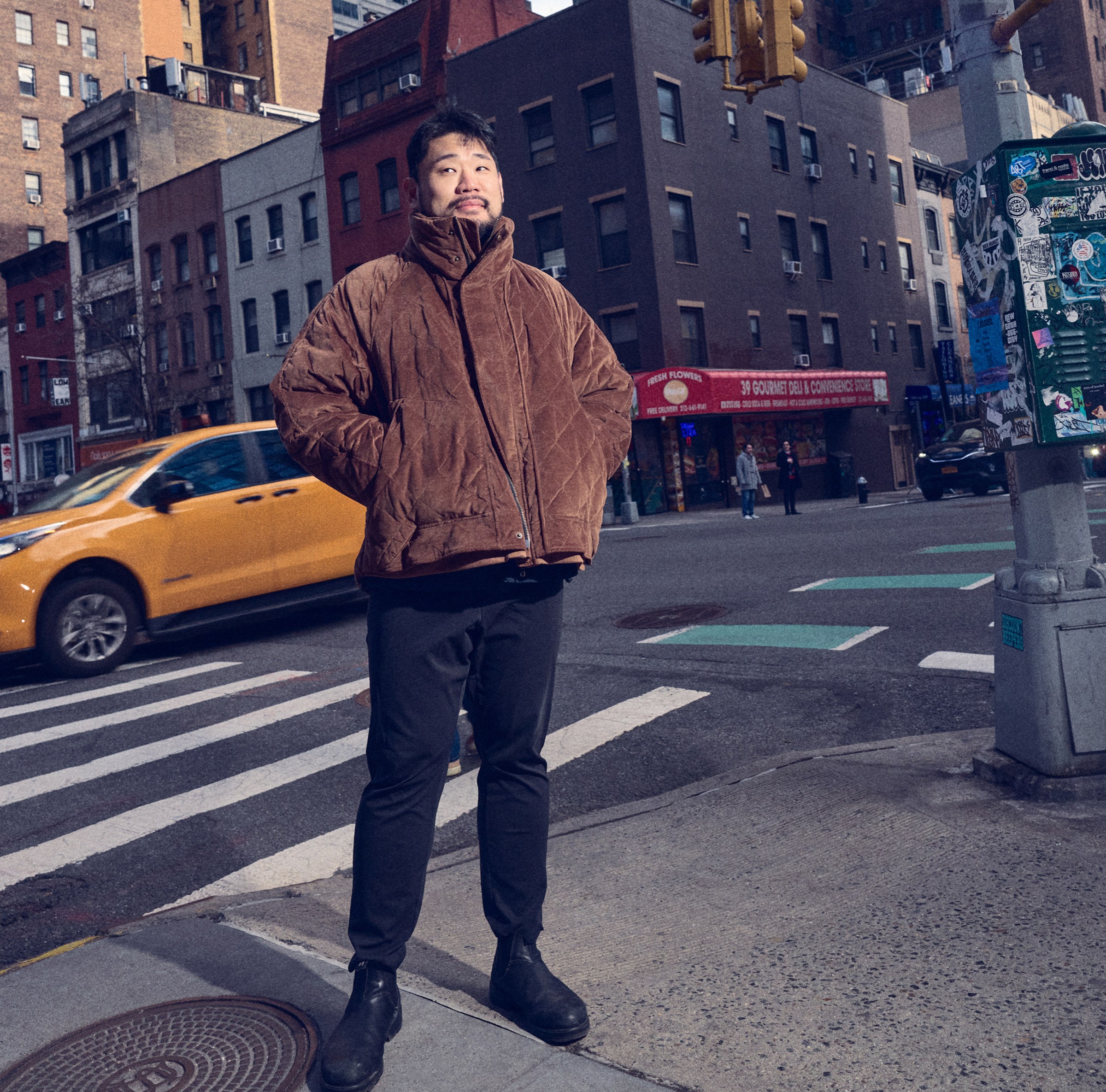 A man in a brown coat and black pants standing outside in a city.