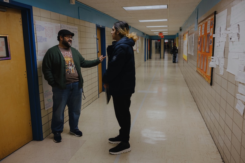 A photograph of an adult educator on the left talking with an adult high school student in a school hallway.