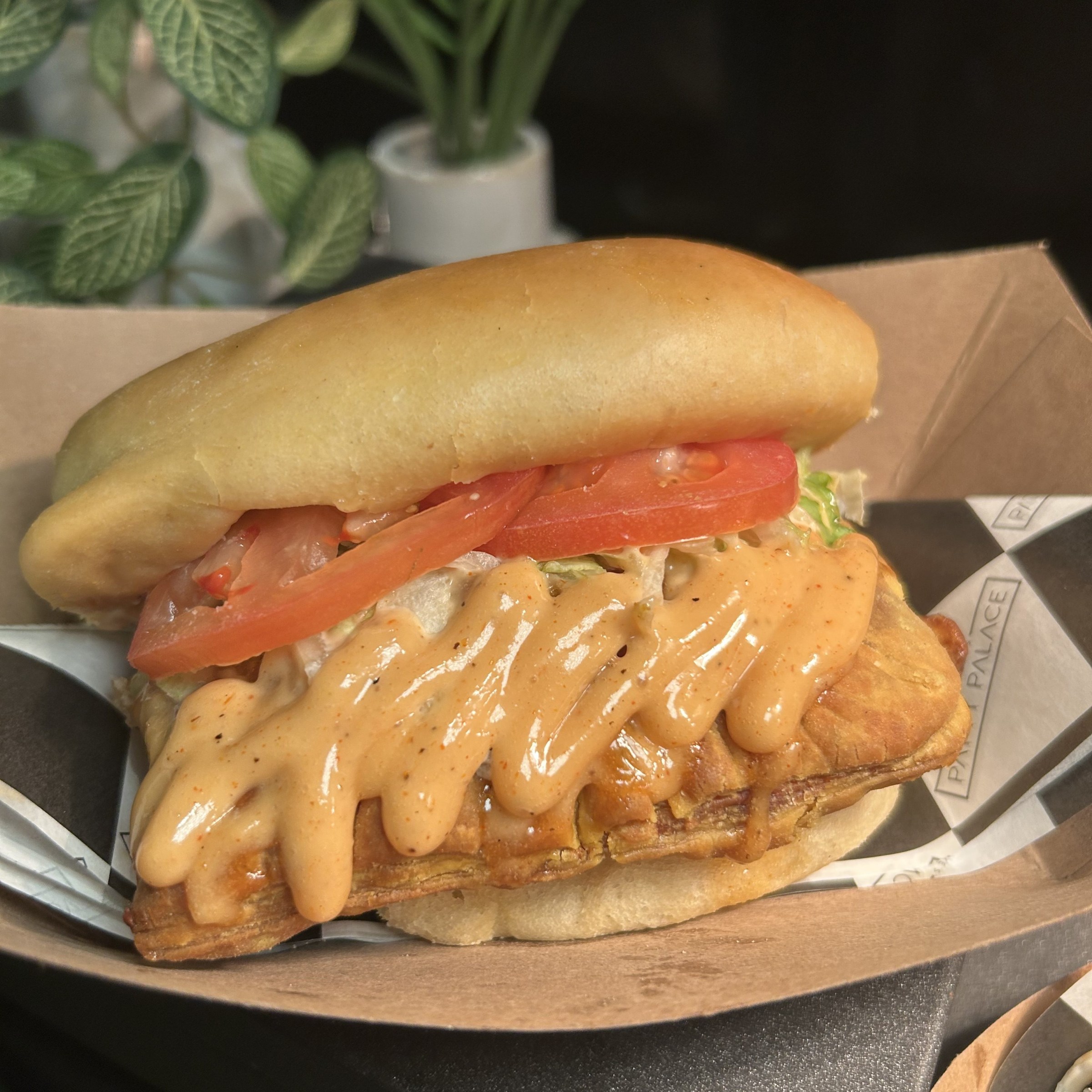 A Jamaican patty with sauce and tomatoes in a bun.