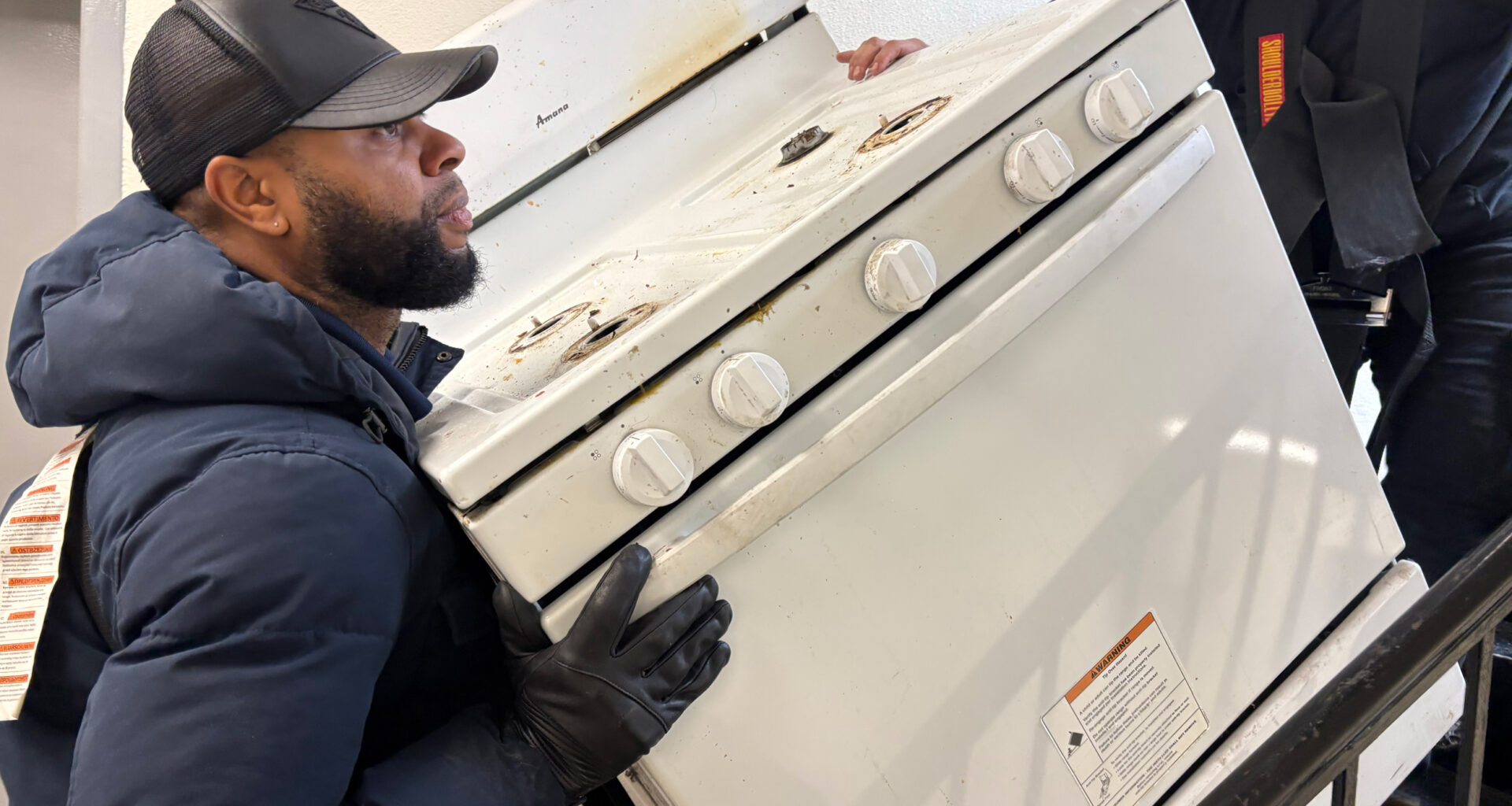 Workers remove an old stove from a Bronx apartment as part of a full-building induction stove installation in New York City. Credit: Lauren Dalban/Inside Climate News
