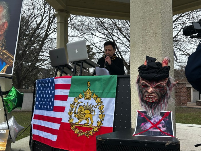 Activist Farshid Dror Bakhshi speaks at the protest beside a demon mask with a turban fixed to the top and a picture of former Supreme Leader Ayatollah Ali Khamenei.