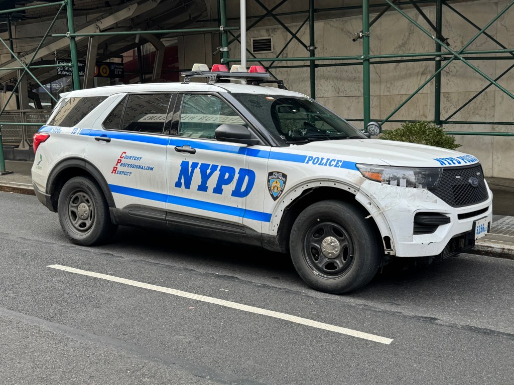An NYPD police vehicle parked near a subway station with construction scaffolding.