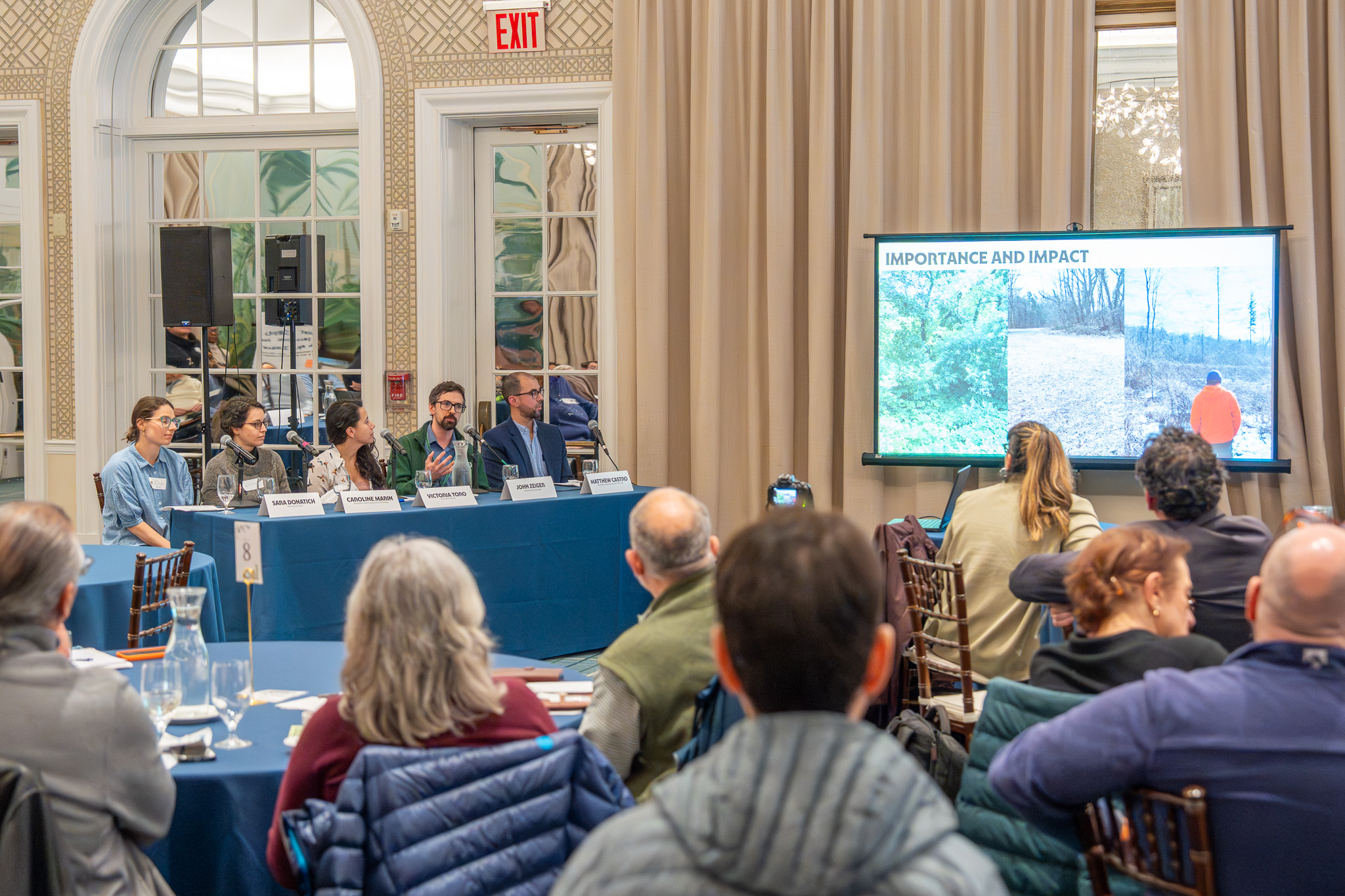 A panel of scientists and practitioners sits in front of a crowd, each person taking time to speak.