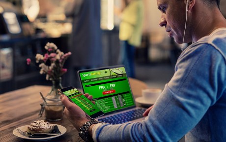 Man using online sports betting services on phone and laptop