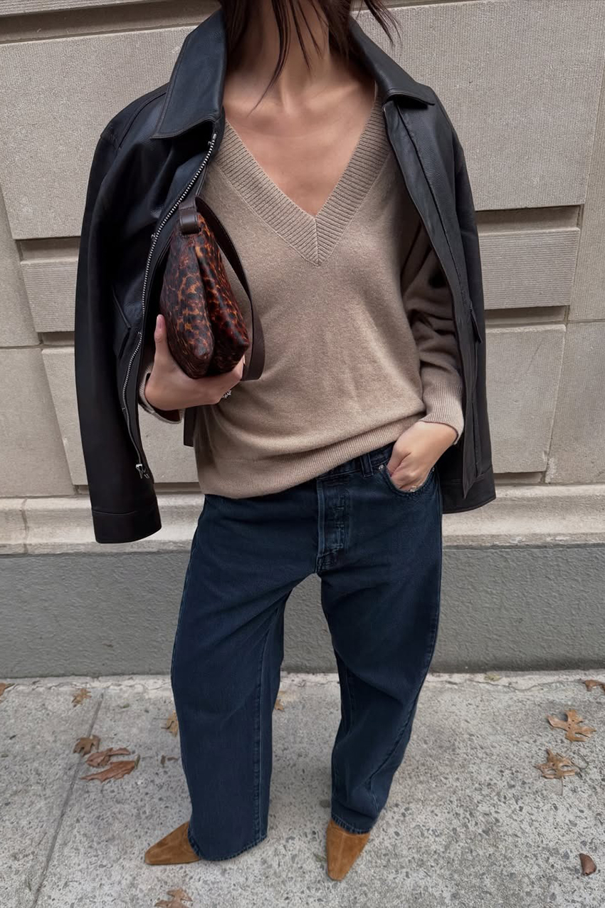 a woman wearing a black leather jacket, V-neck sweater, jeans, and tan boots