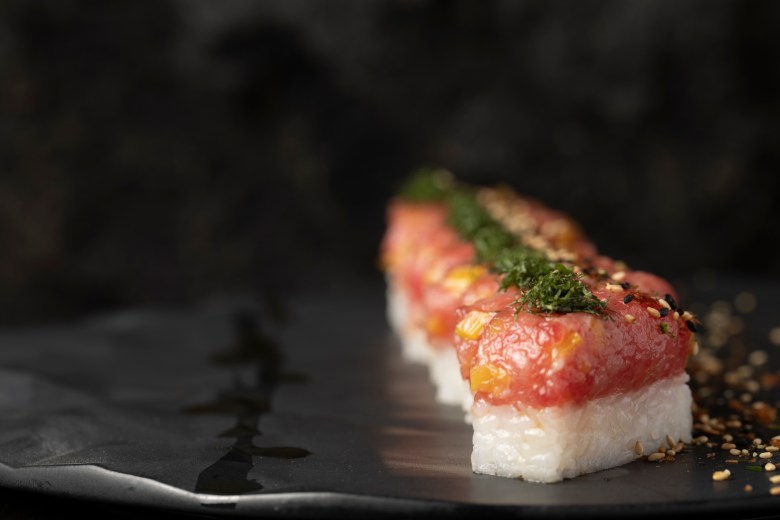 Otoro sushi row on dark slate plate, topped with sesame seeds and microgreens, upscale Japanese restaurant dining