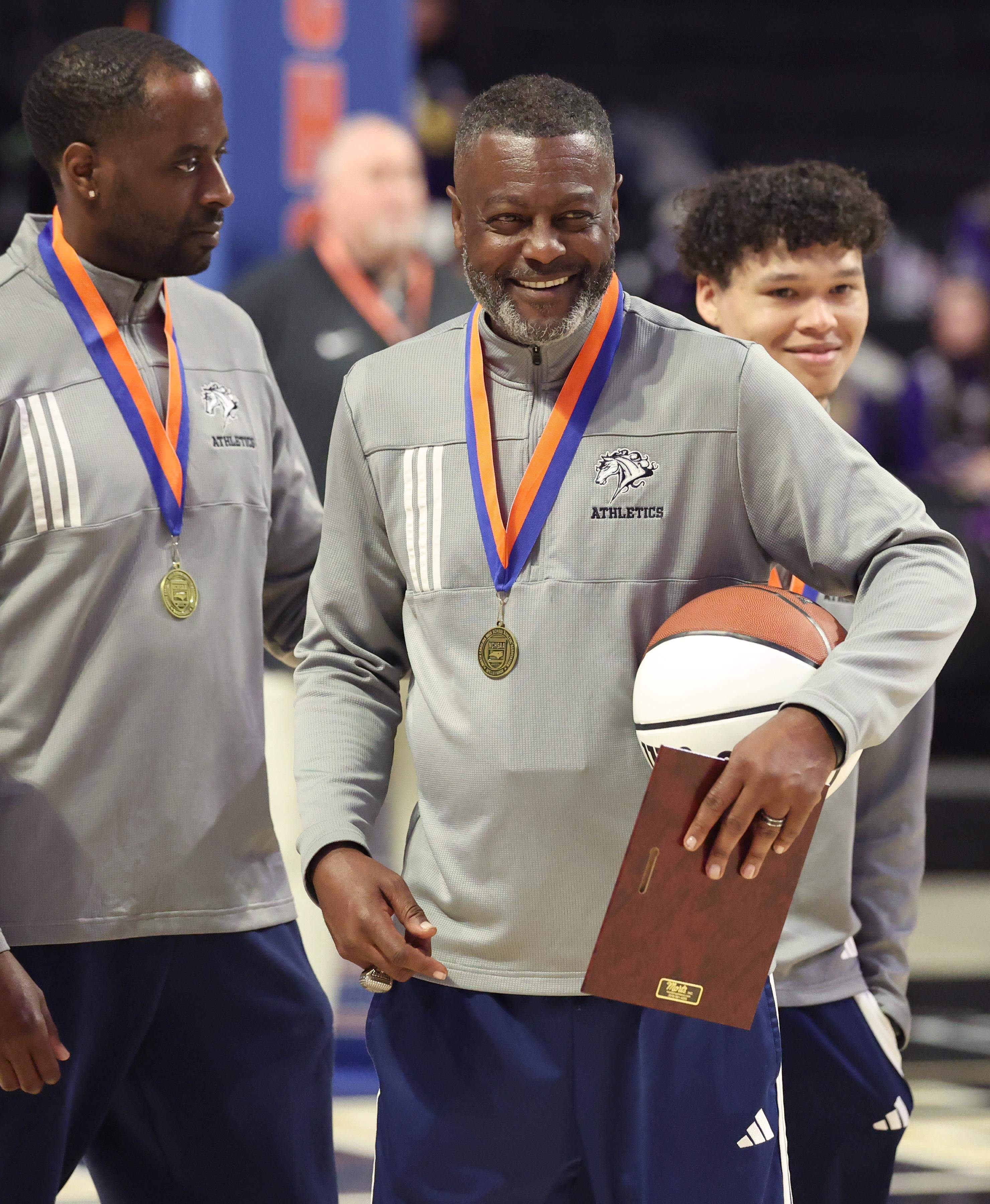 Queen’s Grant head boys’ basketball coach Joe Badgett smiles as his team receives their medals following their 77-43 win over Warren County in the NCHSAA 2A boys’ championship game at Lawrence Joel Veterans Coliseum in Winston-Salem, NC on Thursday, March 12, 2026.