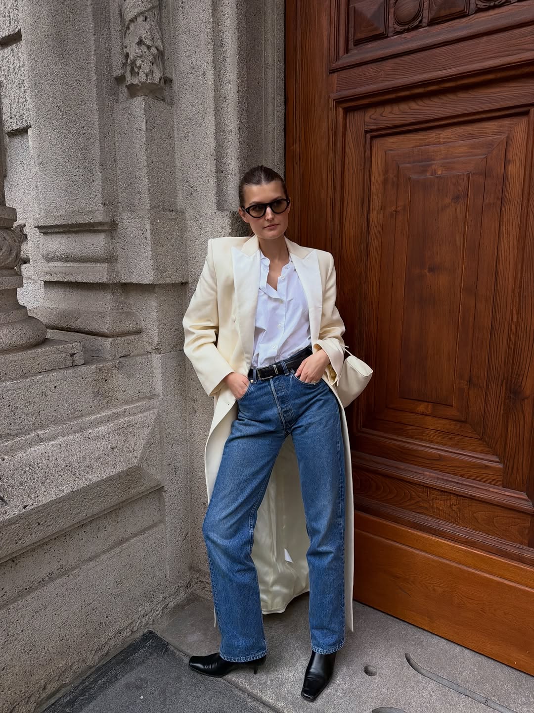 Woman wearing a white button-down, jeans, and a long white coat.