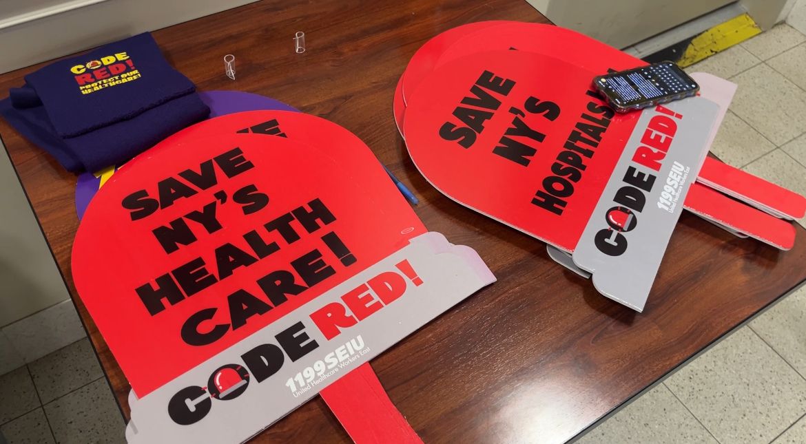 Red paddles that say "SAVE NY'S HEALTHCARE!"