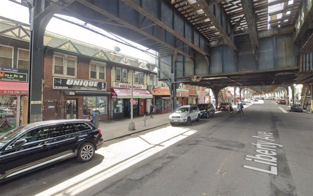 Street view of 109-12 Liberty Avenue in South Richmond Hill, NY, showing a brick building with a hair salon and restaurant under an elevated train track.