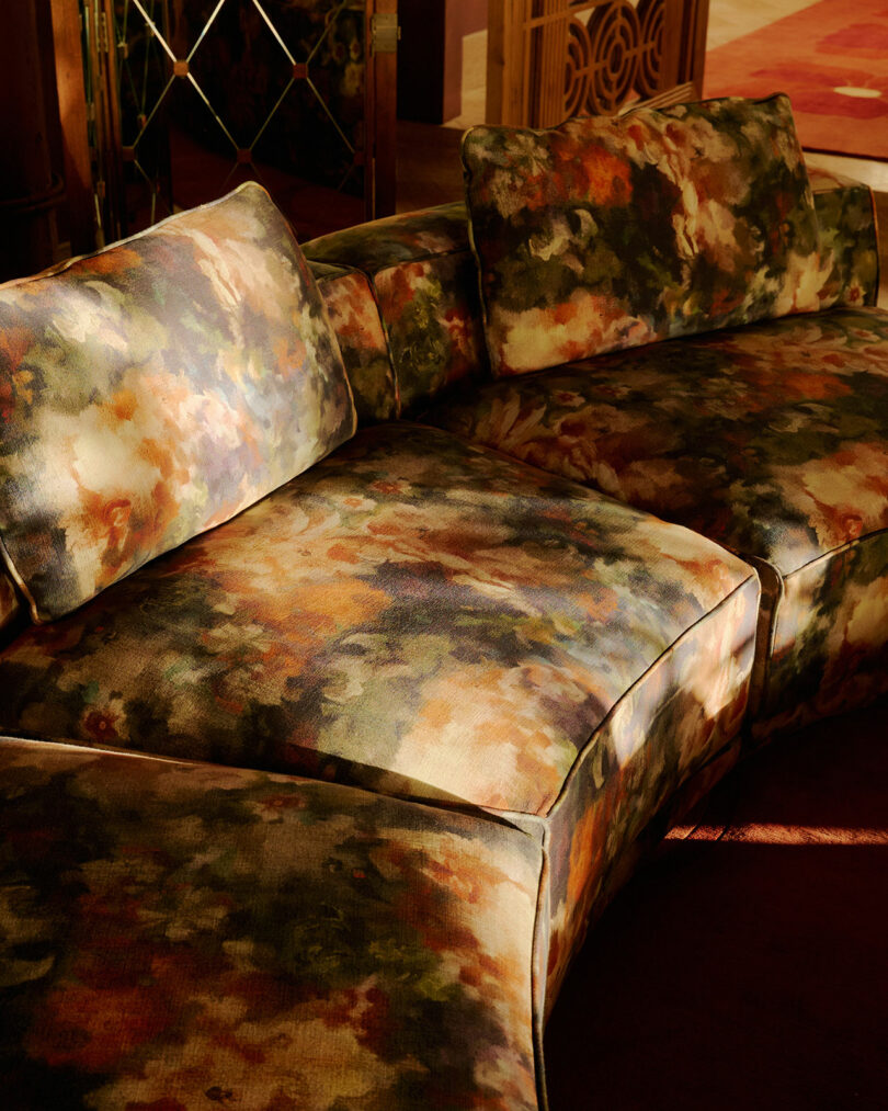 A sectional sofa with abstract, multicolored upholstery in shades of green, orange, and brown, positioned in a warmly lit room.