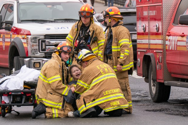 (The woman seen here could be heard shouting in anguish "No, my baby, my baby, I want to see my baby" followed by repeats of "I want to see my baby". She then hopped off the gurney and fought with Medics to get away, whereupon she headed back to the fire scene before being intercepted by Medics, with several Medics eventually needed to hold her down) Three people were killed, including a child of unknown age, with several others suffering serious injuries, after a four-alarm fire broke out inside a two story residence at 44-49 College Point Boulevard in Queens on Monday March 16, 2026. 1309. (Theodore Parisienne / New York Daily News)