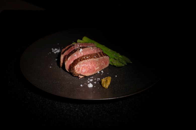 Sliced medium-rare steak with sea salt flakes, asparagus, and mustard on a dark plate at Umi in Atlanta