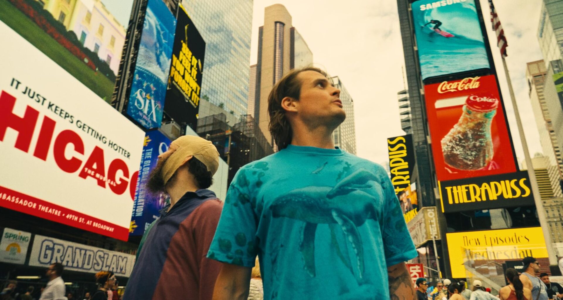 Two people stand in Times Square looking up, surrounded by buildings and signs