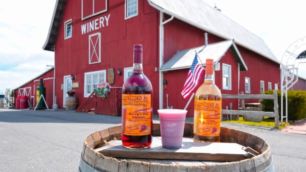 Wine bottles sitting on a barrel outside of a red barn