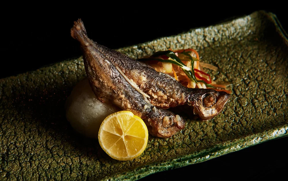 A roasted fish on a green tray next to a yellow fruit.