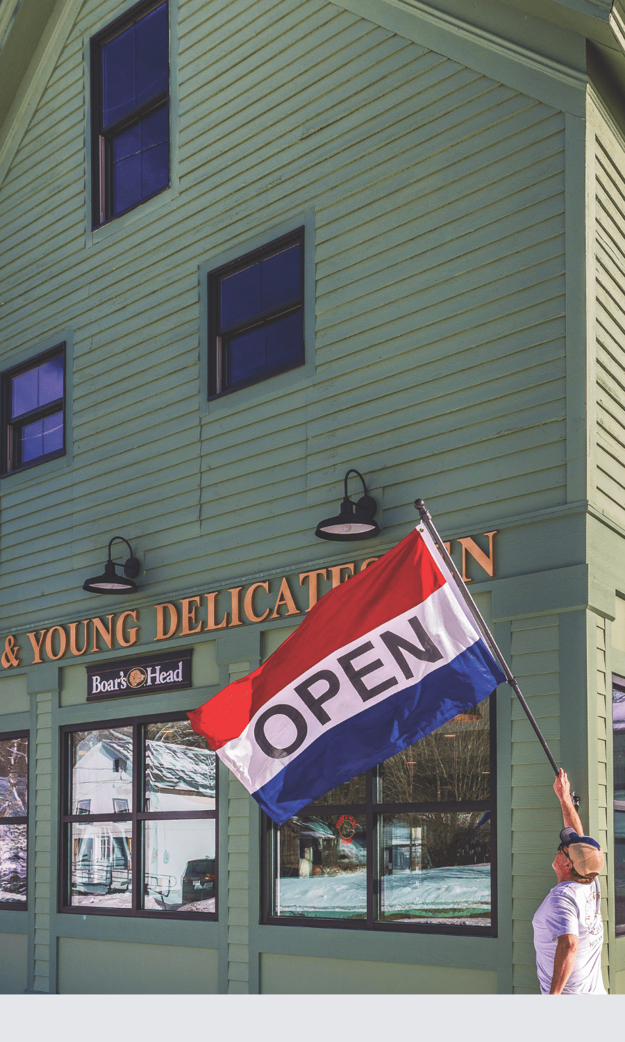 Man hangs “open” flag outside green building with windows and wylde & young name on front