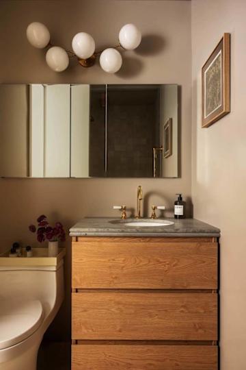 Modern bathroom featuring a wooden vanity with a marble countertop, gold faucets, and a wall-mounted light fixture.
