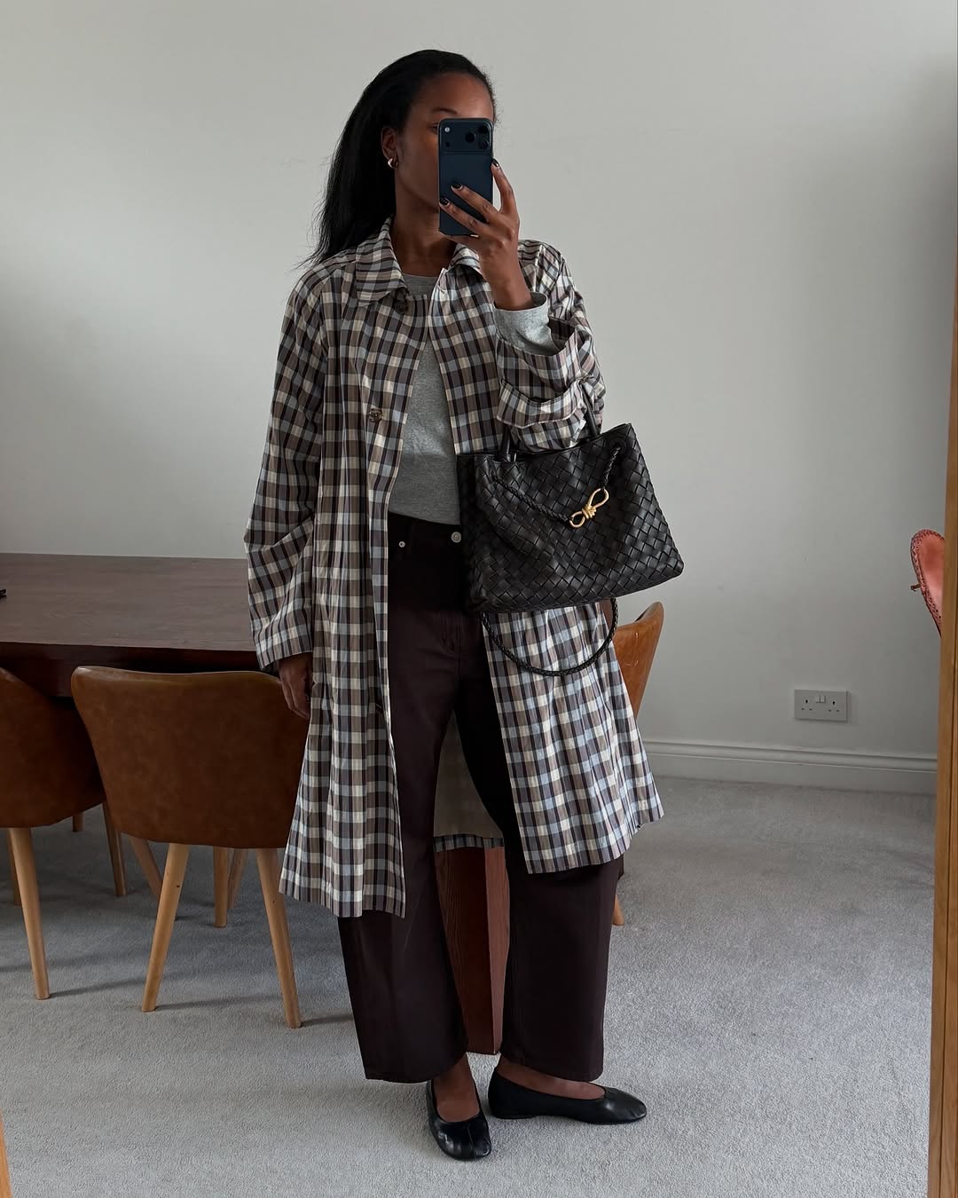 Woman wearing a long plaid coat, dark jeans, and black ballet flats.