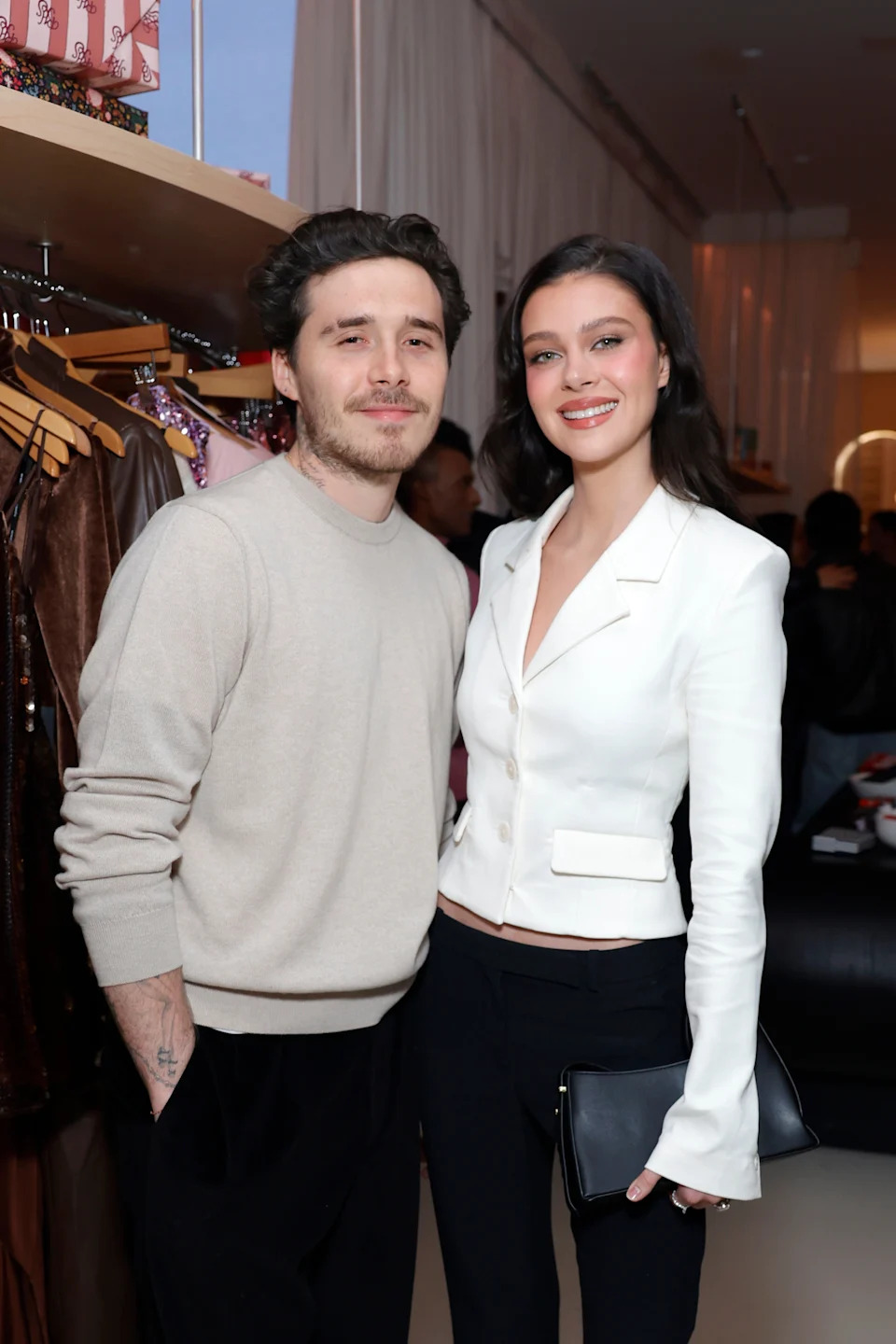 Brooklyn Beckham wearing a casual sweater and Nicola Peltz Beckham in a stylish tailored blazer, pose together at an event