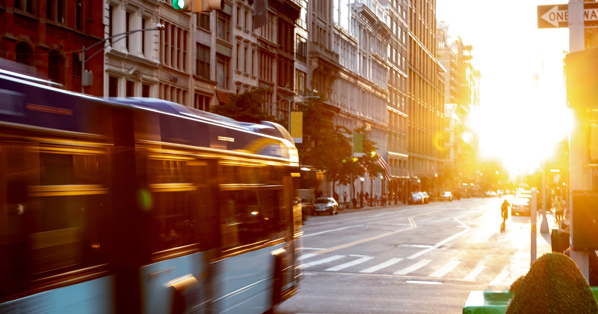 New York City bus driving through the intersection of 23rd Street and 5th Avenue in Manhattan with the light of sunset shining between the skyline buildings.