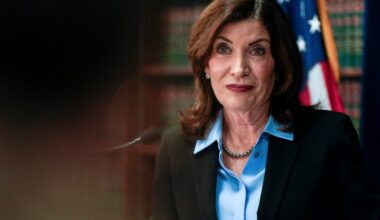 A woman looking serious wearing a dark jacket and a blue shirt.