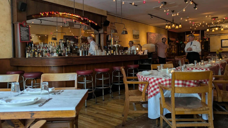 A view of the interior of Noodle Pudding, showing tables with red-checkered tablecloths and a large bar.