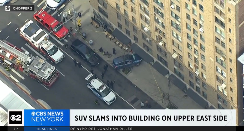 Aerial view of an SUV that has crashed into the GINETTE NY jewelry store with emergency vehicles and personnel on the street.