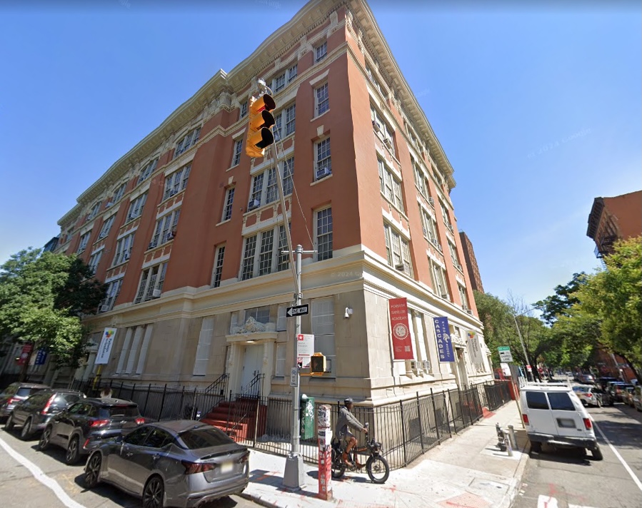 The exterior of Cascades High School, a large red brick building with many windows and cars parked along the street.