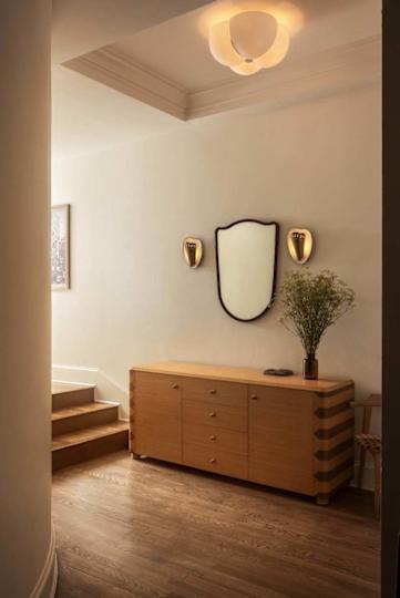 A warm-toned hallway featuring a wooden sideboard with drawers, a mirror, wall sconces, and a vase of flowers.