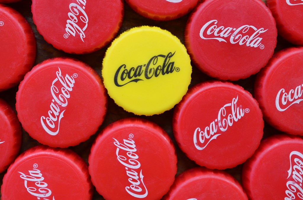 Multiple red Coca-Cola bottle caps surrounding one yellow Coca-Cola bottle cap.
